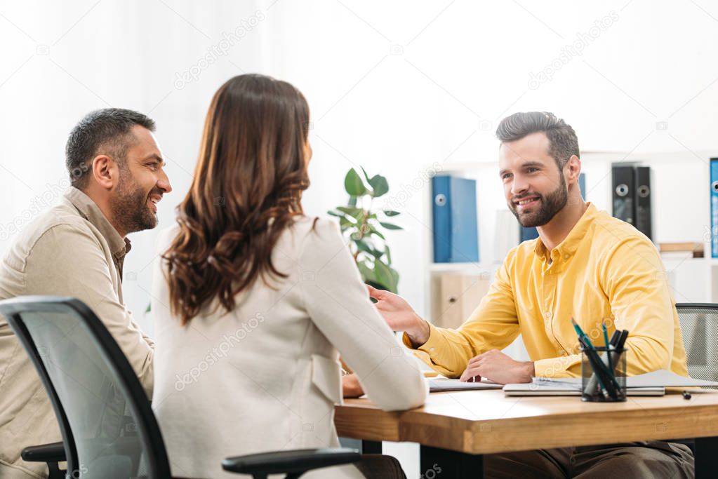 advisor sitting at table and smiling to man and woman in office
