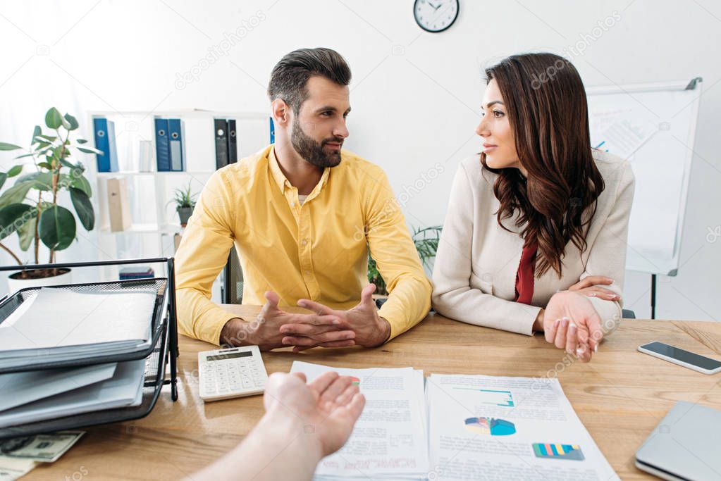 investors sitting at table and talking wile advisor pointing at documents with hand in office