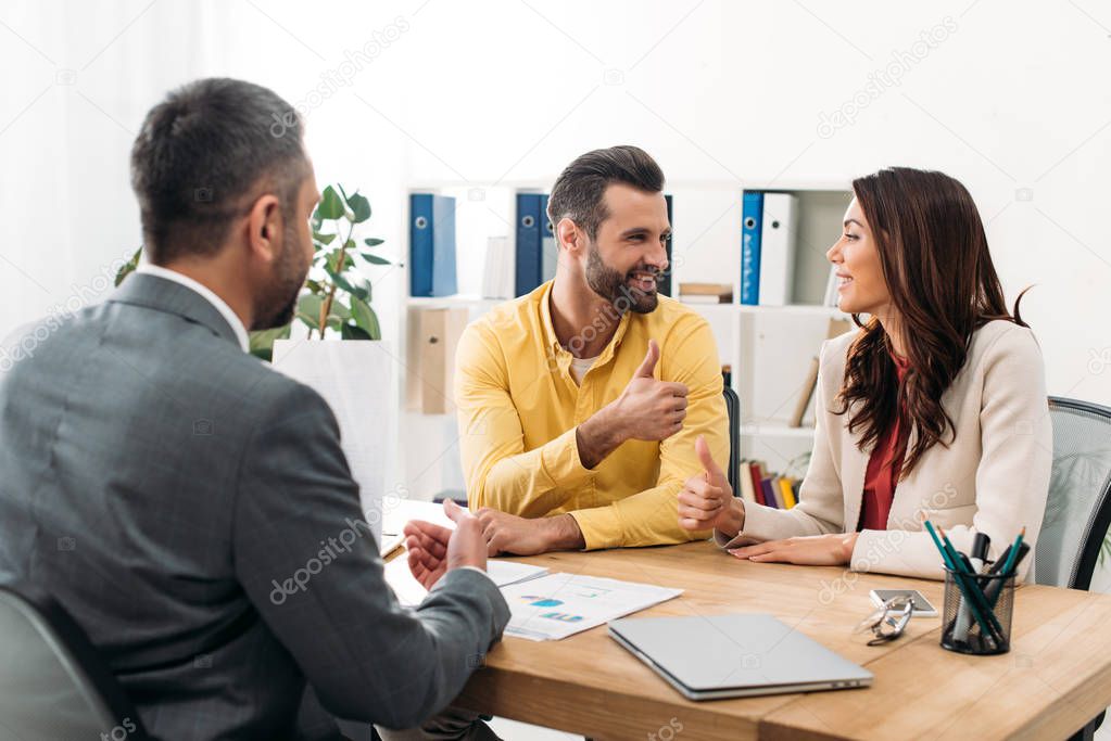 investors sitting at table and thumbing ups near advisor in office