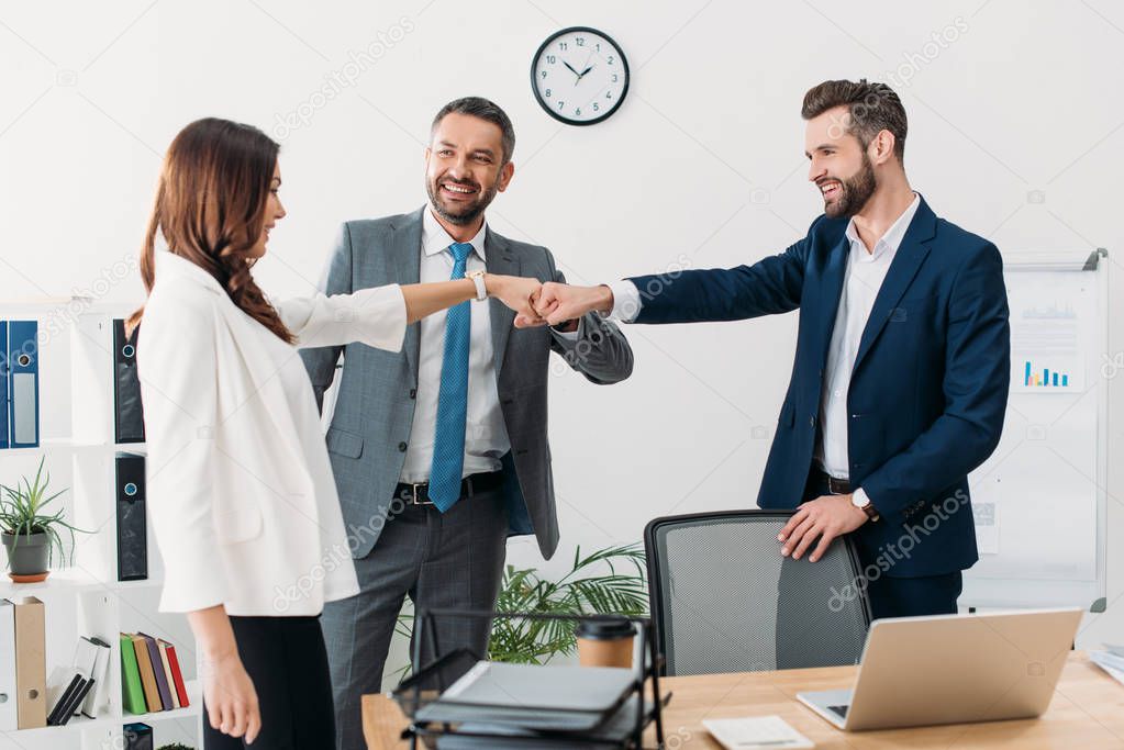colleagues standing near table, smiling and celebrating in office