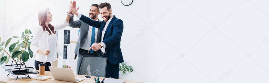 colleagues at table with laptop smiling and highing five in office