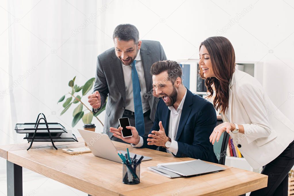 colleagues at table looking to laptop and rejoicing in office