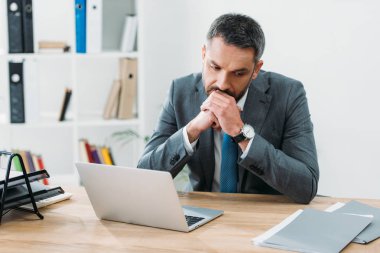 laptop ile masada oturan ve ofiste düşünme yakışıklı işadamı