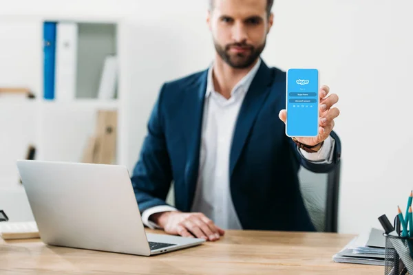 Foco Seletivo Empresário Sentado Mesa Com Laptop Mostrando Smartphone Com — Fotografia de Stock