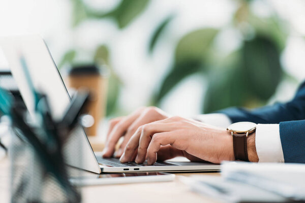 cropped view of businessman at table with laptop and typing in office