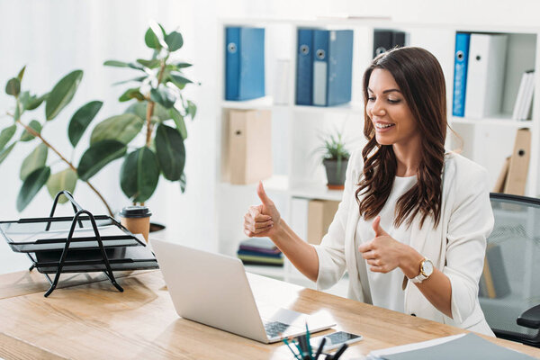 businesswoman sitting at table with laptop and thumb ups in office