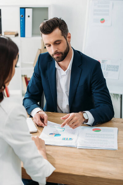 selective focus of handsome advisor showing and pointing with finger to document 