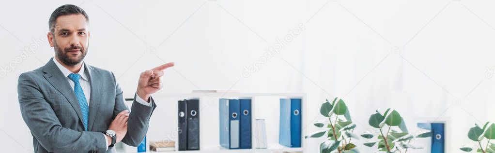 handsome businessman standing and pointing with finger to side in office