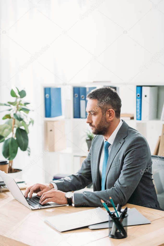 handsome and focused advisor in suit using laptop at wokspace 