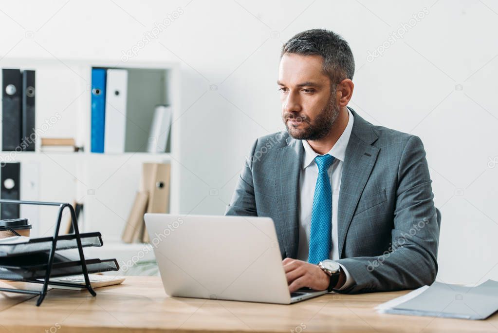 concentrated and focused advisor in suit using laptop at wokspace 