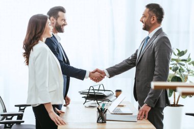 handsome advisor in suit shaking hands with investors at workplace   clipart