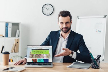 bbc Web sitesinde office ekranında olan dizüstü bilgisayar, parmaklarıyla işaret takım elbiseli yakışıklı Danışmanı 