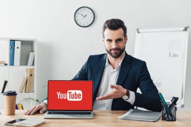 laptop ile youtube Web sitesinde office ekranında, parmaklarıyla işaret takım elbiseli yakışıklı Danışmanı 