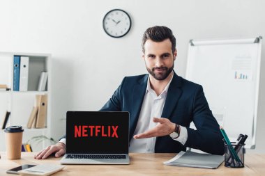 laptop ile netflix Web sitesinde office ekranında, parmaklarıyla işaret takım elbiseli yakışıklı Danışmanı 