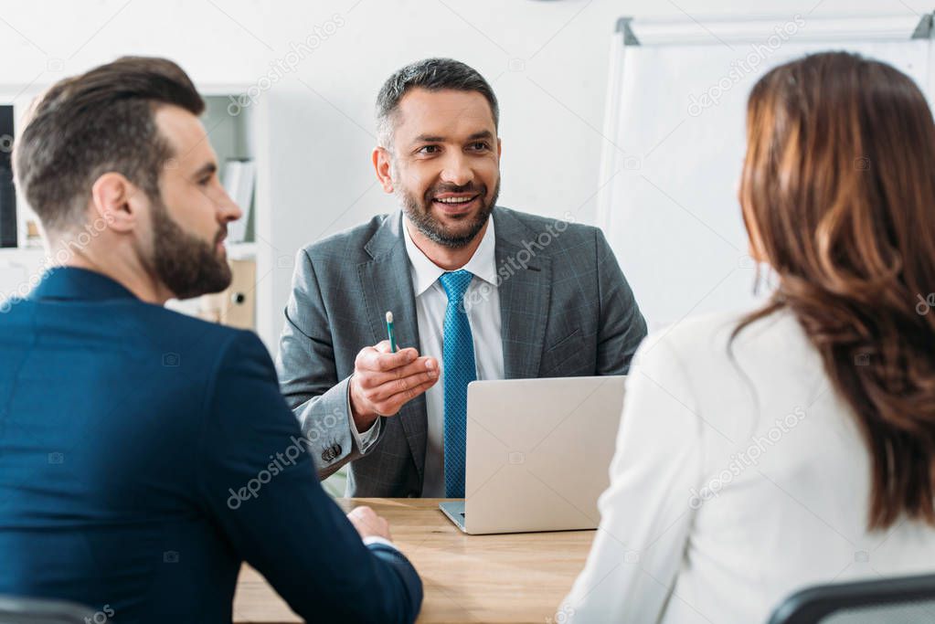 selective focus of handsome advisor in suit talking with investors at office 