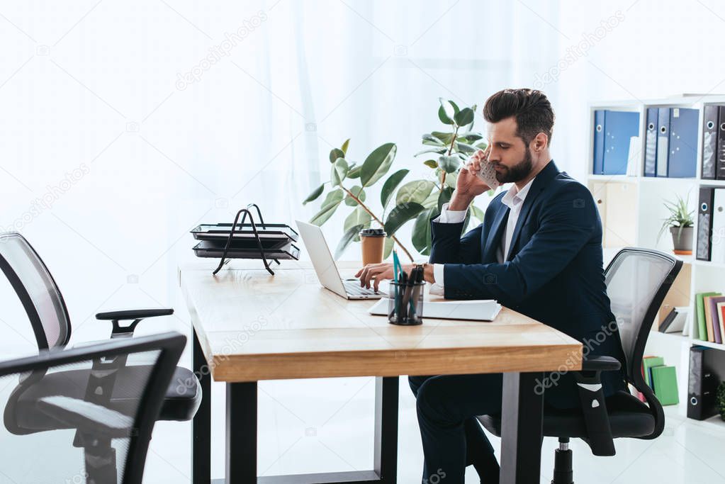 handsome advisor in suit talking on smartphone at workspace 