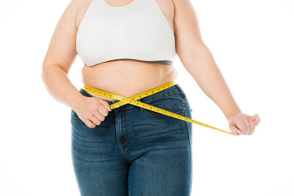 cropped view of overweight woman  in jeans measuring waist with measuring tape isolated on white, lose weight concept
