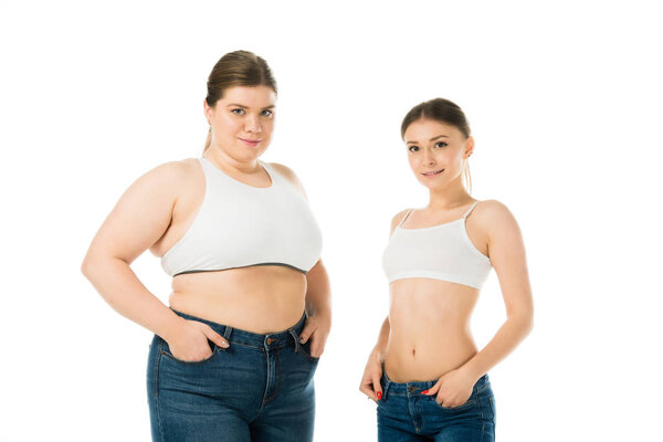 smiling overweight and slim women posing with hands in pockets isolated on white, body positivity concept