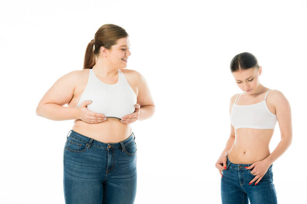 sad slim and happy overweight women in denim posing together isolated on white, body positivity concept 