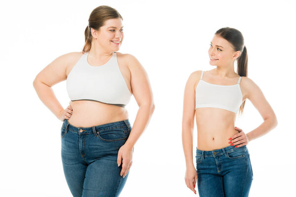 smiling slim woman looking at overweight woman in denim isolated on white, body positivity concept 