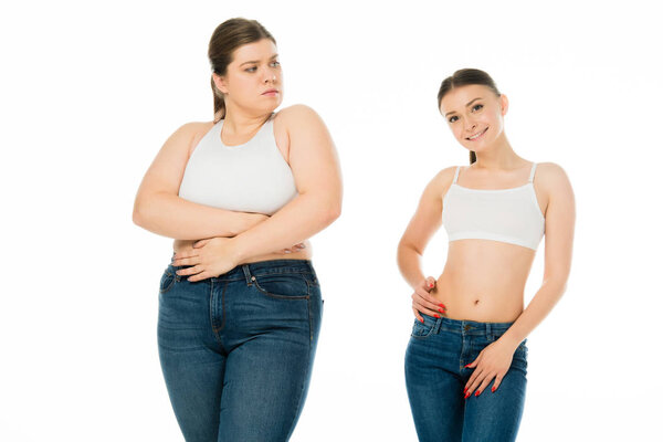 sad overweight woman covering body with hands and looking at slim happy woman isolated on white