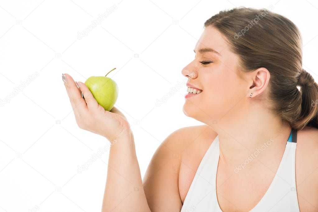young smiling overweight woman looking at green apple isolated on white