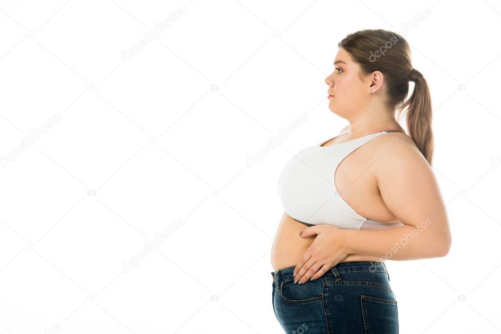 side view of overweight woman in denim posing with hand on belly isolated on white