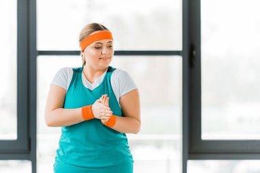 overweight woman standing in sportswear and warming hands clipart