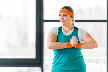 smiling overweight woman standing in sportswear and warming hands clipart