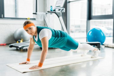 kilolu kız tahta egzersiz fitness mat yaparken kameraya bakıyor 