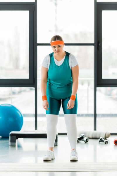 upset overweight woman standing in sportswear in gym