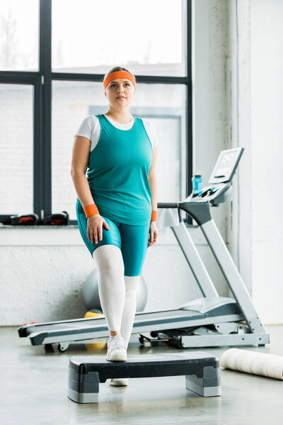 attractive plus size girl standing on step platform in gym