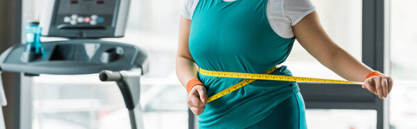 cropped view of plus size girl measuring waist in gym
