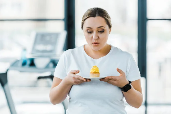 超重的女人看着美味的纸杯蛋糕在健身房 — 图库照片
