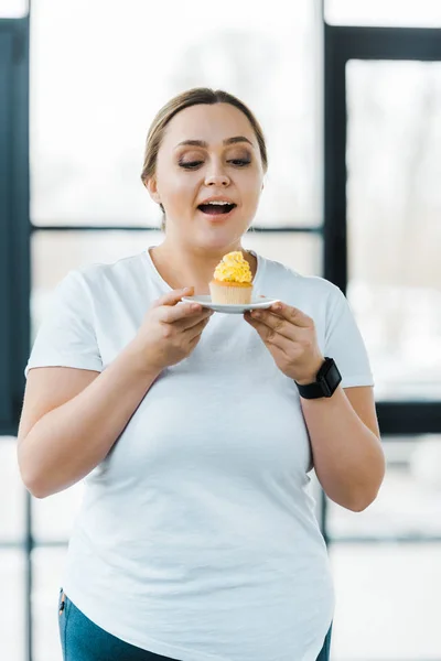 快乐超重的女人看着美味的纸杯蛋糕在健身房 — 图库照片