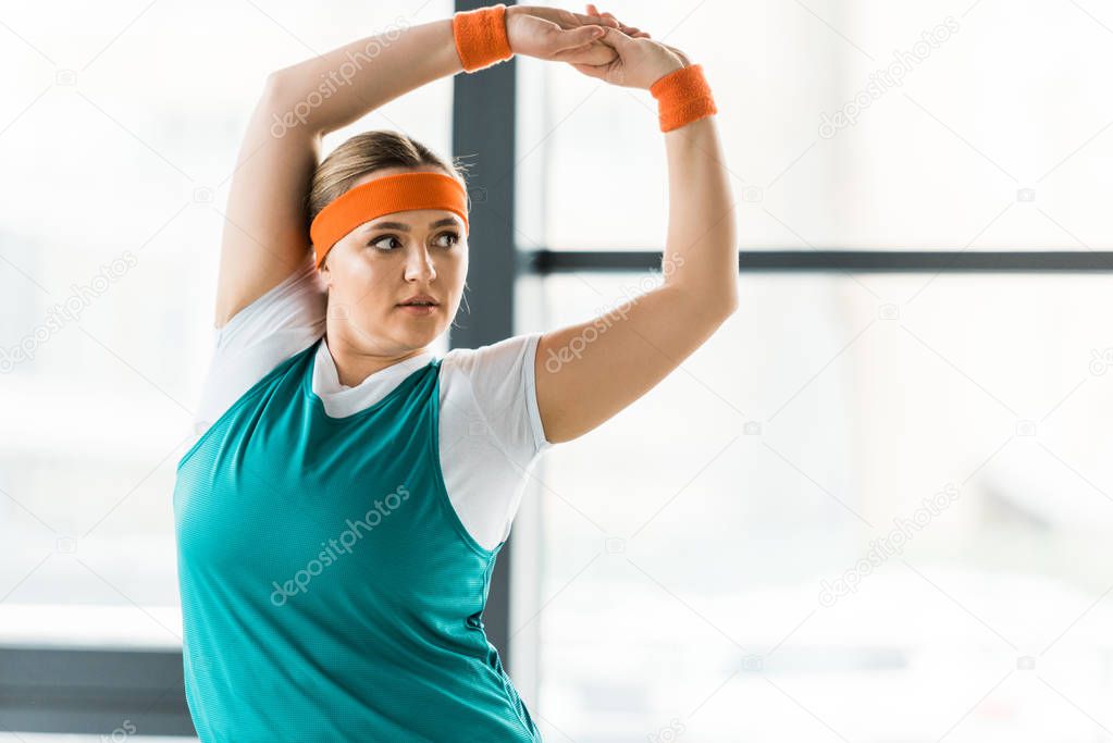 overweight woman stretching while standing in sportswear in gym