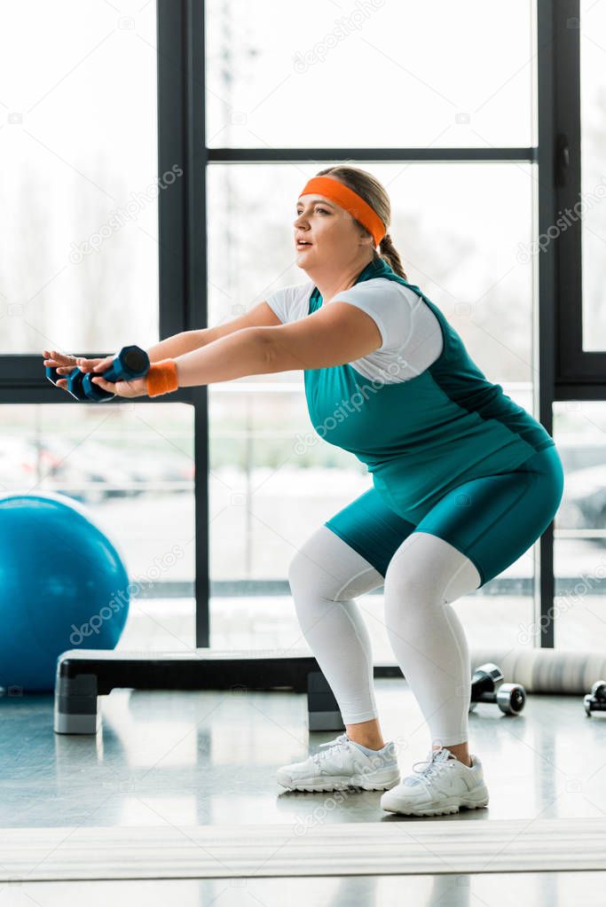 attractive overweight woman exercising with dumbbells in gym