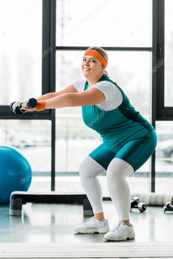 happy plus size woman exercising with dumbbells in gym