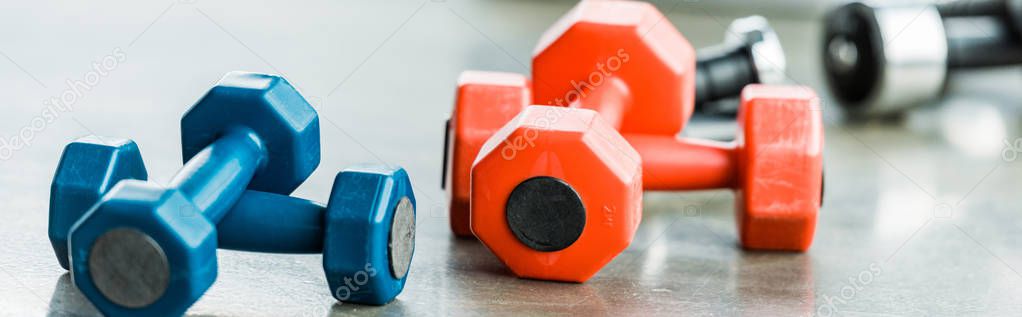 selective focus of heavy metallic multicolored fitness dumbbells in gym