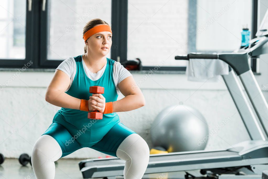attractive overweight girl squatting with dumbbell in gym