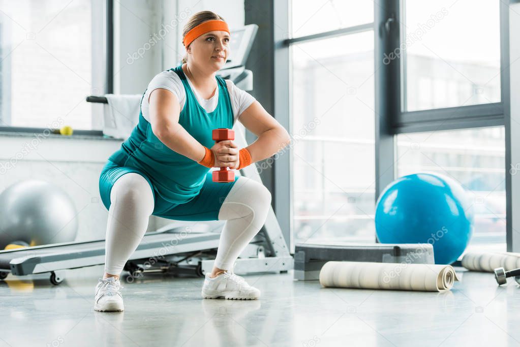 happy overweight girl squatting with dumbbell in gym