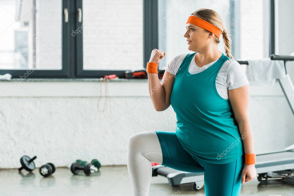 attractive overweight girl in sportswear squatting in gym