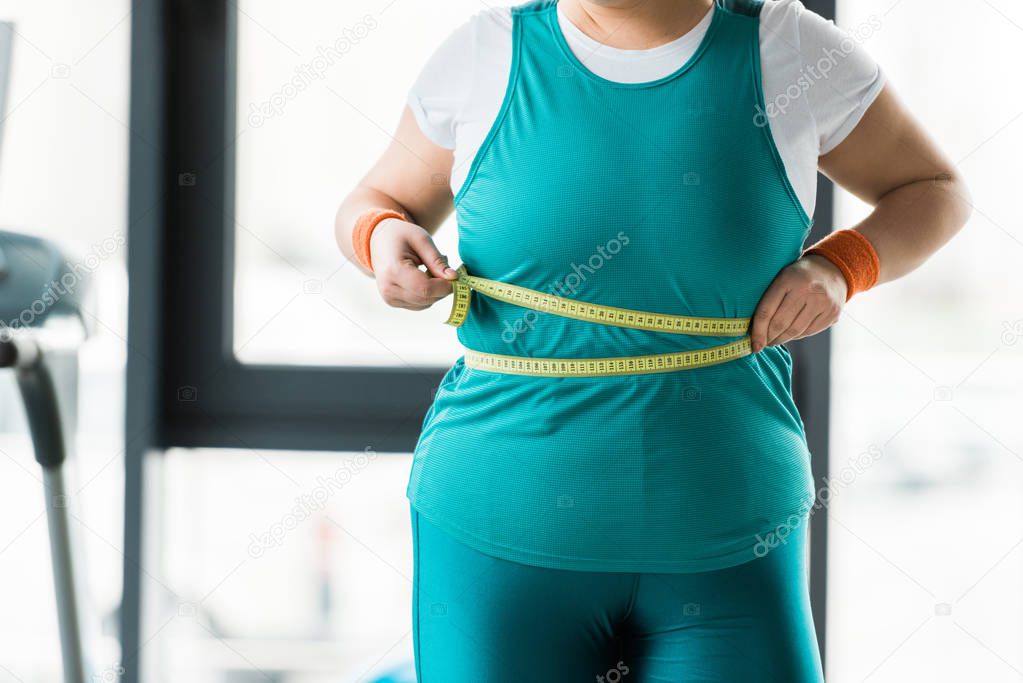 cropped view of overweight girl measuring waist in gym