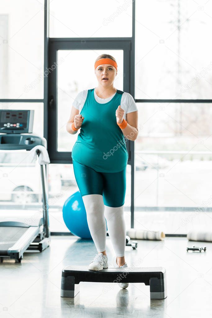 overweight girl exercising on step platform near sport equipment