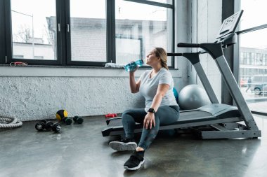 artı boyutu kadın koşu bandı ve içme suyu şişe oturuyordu yorgun