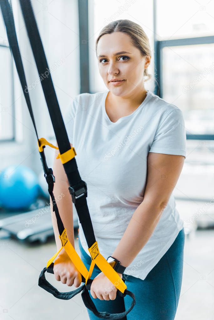 attractive overweight girl training arms with suspension straps in gym