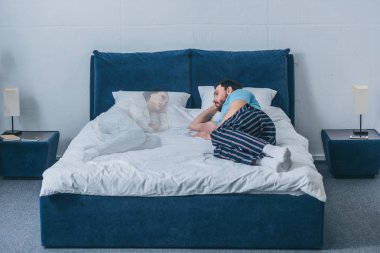 depressed man lying in bed and looking at wife ghost