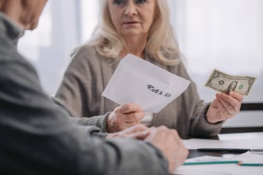 cropped view of senior couple holding envelope with 'roth ira' lettering and dollar banknote clipart