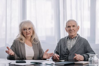 senior couple sitting at table with paperwork and looking at camera clipart