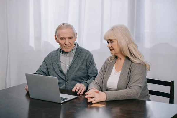 Chateado Casal Sênior Sentado Mesa Usando Laptop Casa — Fotografia de Stock